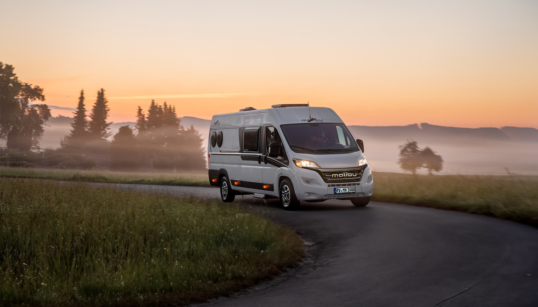 Weißer Malibu Van, fährt auf einer Landstraße außen rum Sonnenuntergang.