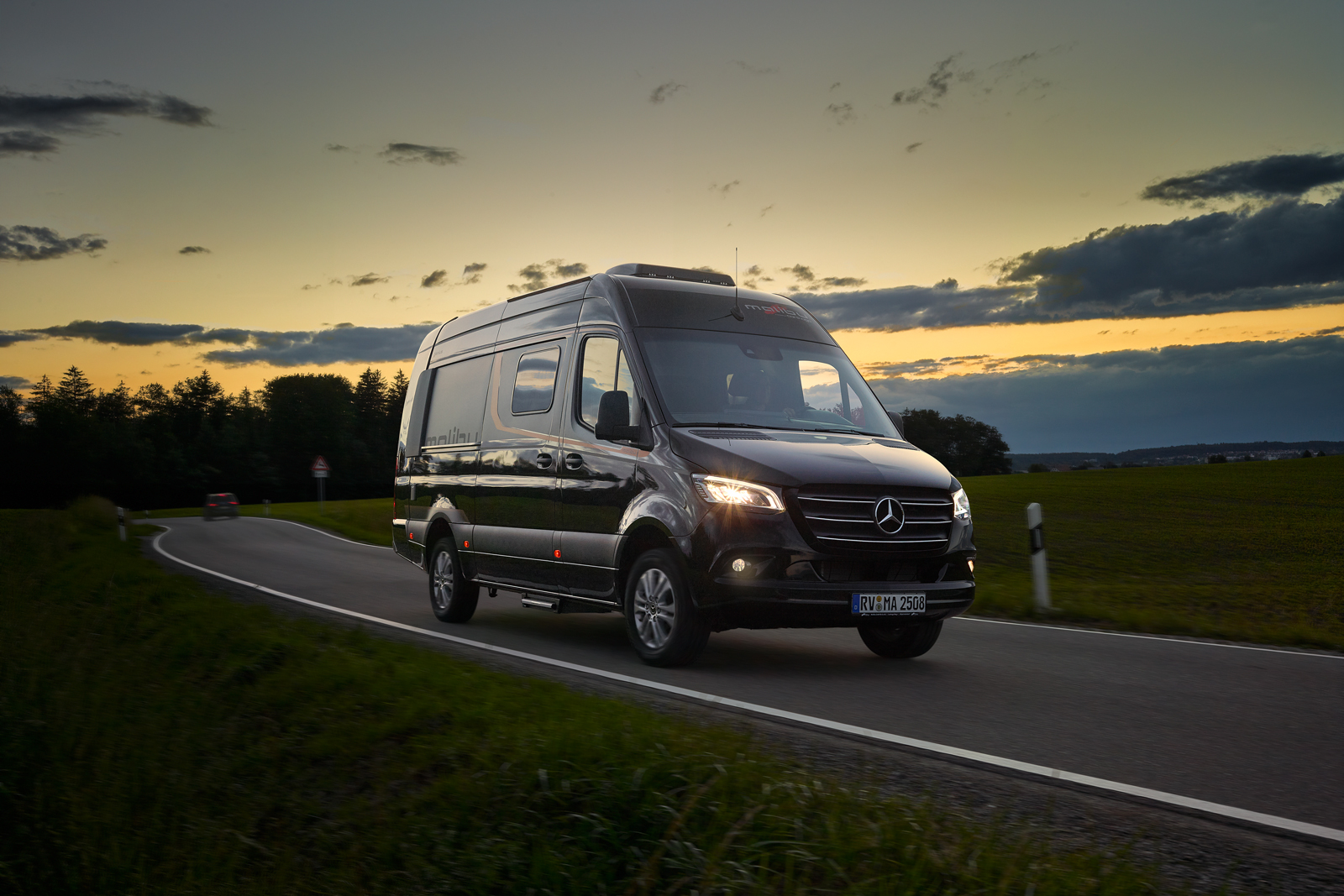 Malibu Genius 641 LE in obsidianschwarzer Farbe, auf einer Landstraße bei Abenddämmerung, umgeben von einer stimmungsvollen Landschaft mit sanftem, goldenem Licht im Hintergrund