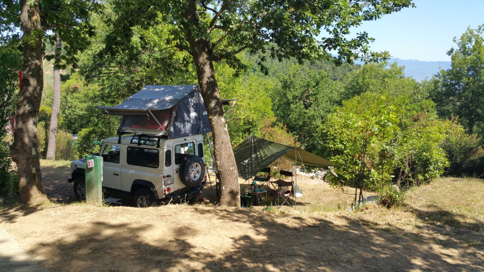 Jeep parkend unter einem Baum in einer trockenen Landschaft umgeben von grünen Büschen und Bäumen auf einem Hügel