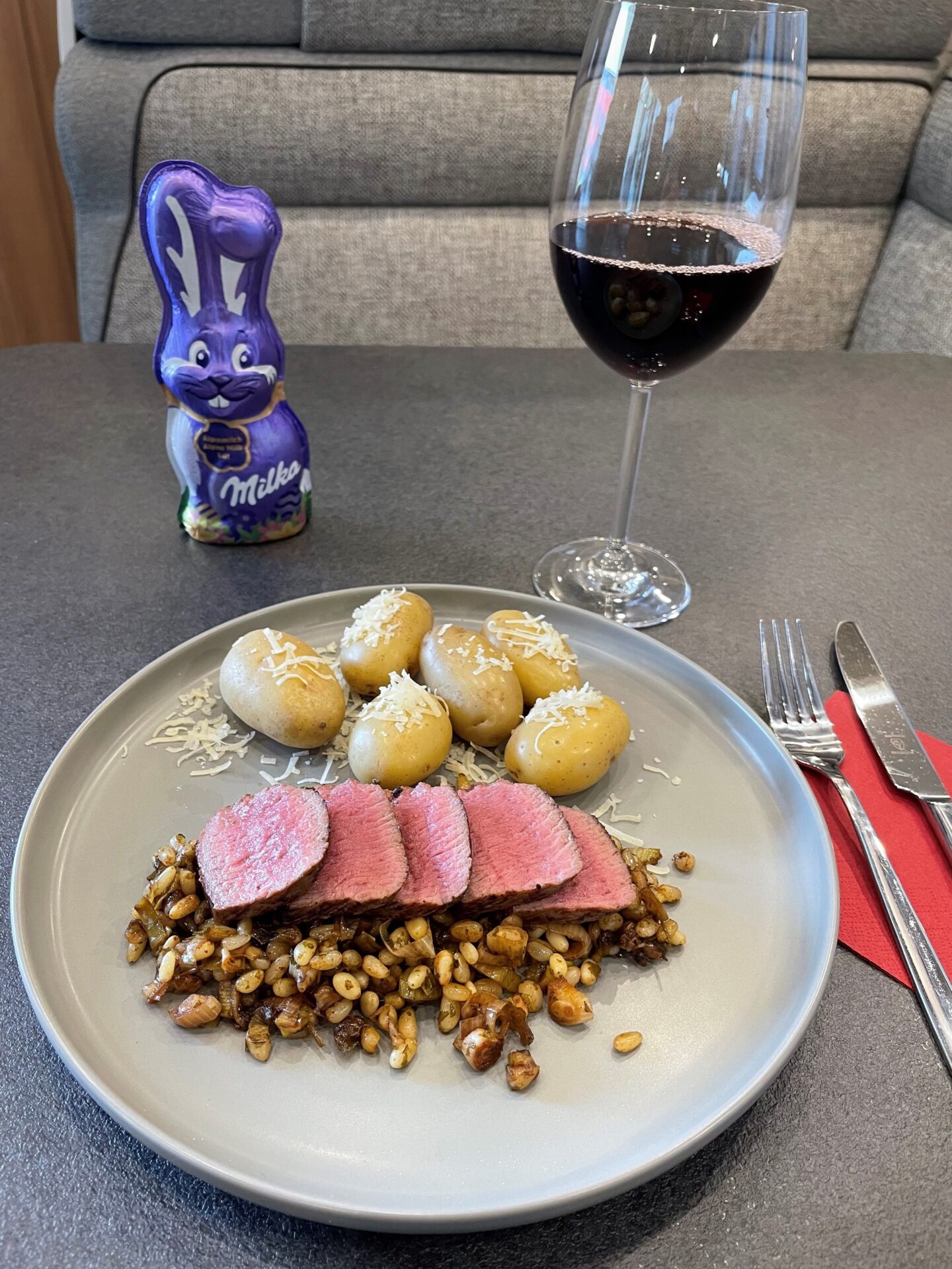 Teller mit Fleisch und Kartoffeln und dahinter ein Osterhase und ein Weinglas.