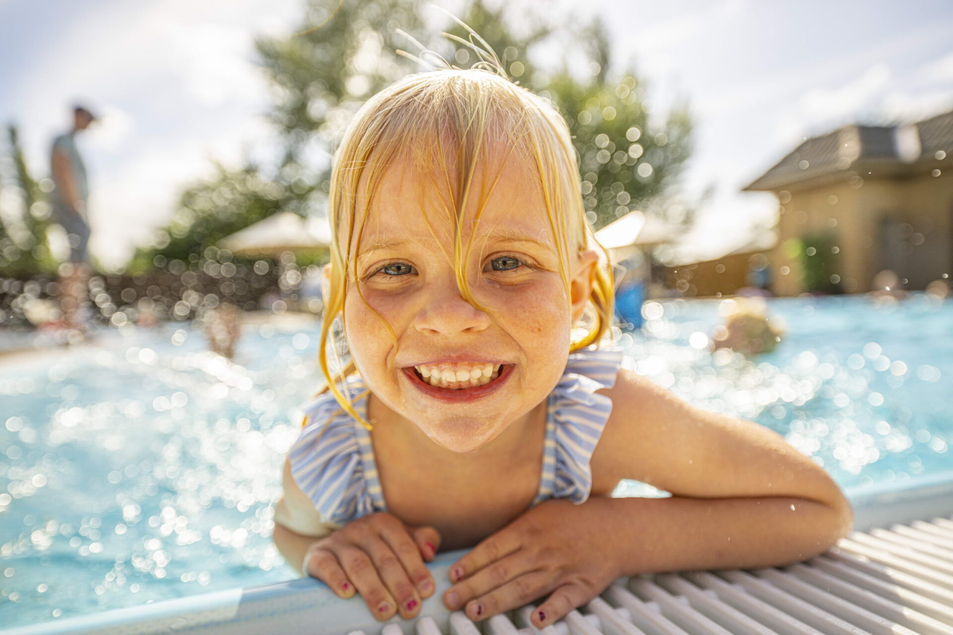 Kleines Mädchen schwimmt in einem Wasserbecken, hält sich am Beckenrand fest und lächelt.