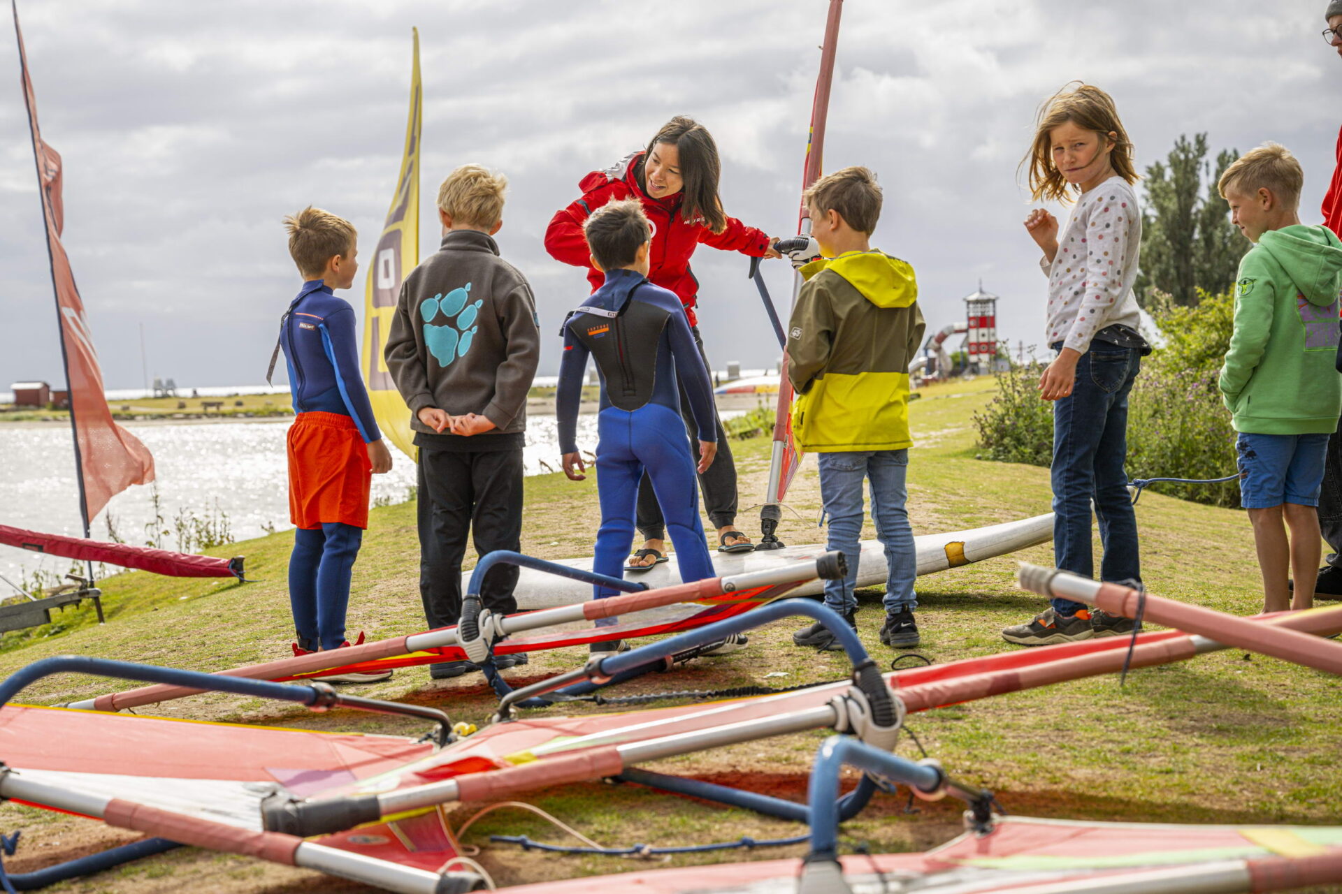 Viele Kinder mit einer Frau, die am Ufer Kitesurfen lernen