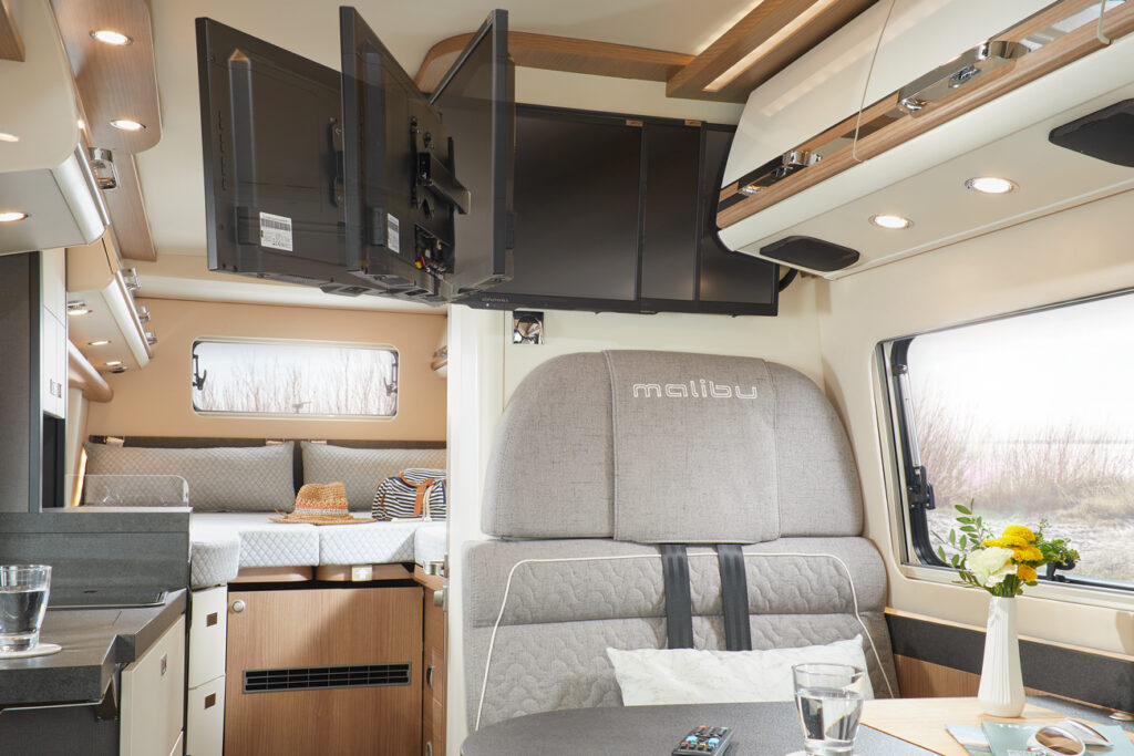 Innenraum Ansicht des Gemütlicher Wohnbereich des Malibu Genius 641 LE, mit stilvollen Polstermöbeln, einem eleganten Tisch und modernen Designelementen, die den Komfort und die integrierte TV Halterung hervorheben