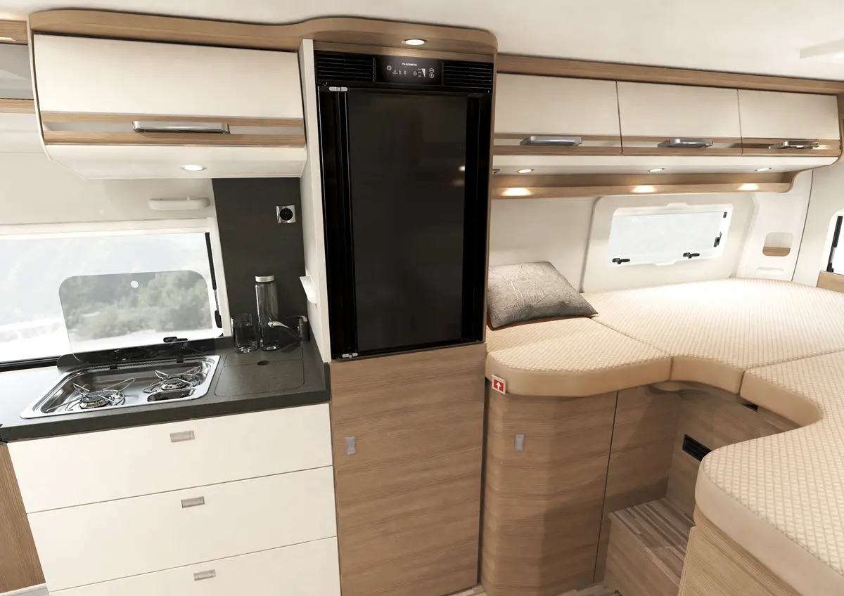 Der stilvolle Innenraum des Malibu Vans kombiniert eine kompakte Küchenzeile mit Gasherd und Spüle, einem eleganten, integrierten Kühlschrank und einem gemütlichen Schlafbereich, alles in hochwertigem Design und harmonischer Holzoptik.