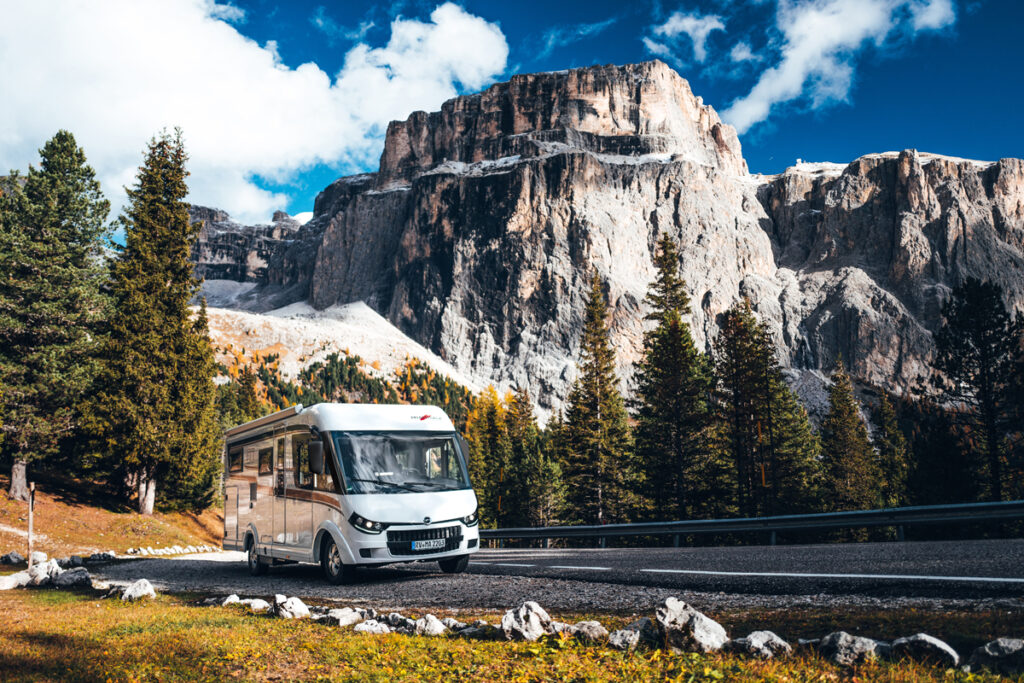 Malibu Wohnmobil in einem Außenbereich, fährt vor einer malerischen Kulisse mit Bäumen und Bergen im Hintergrund, das Fahrzeug zeigt seine moderne, elegante Frontansicht