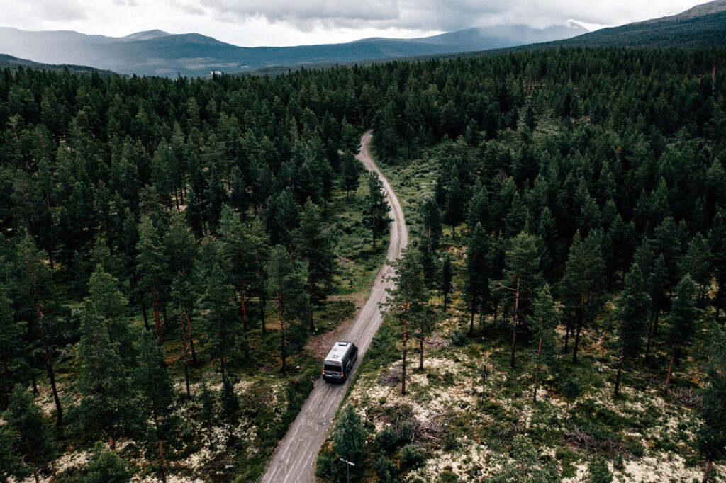 Blick von oben auf ein Malibu Fahrzeug, das allein eine Straße durch einen dichten Wald entlangfährt.