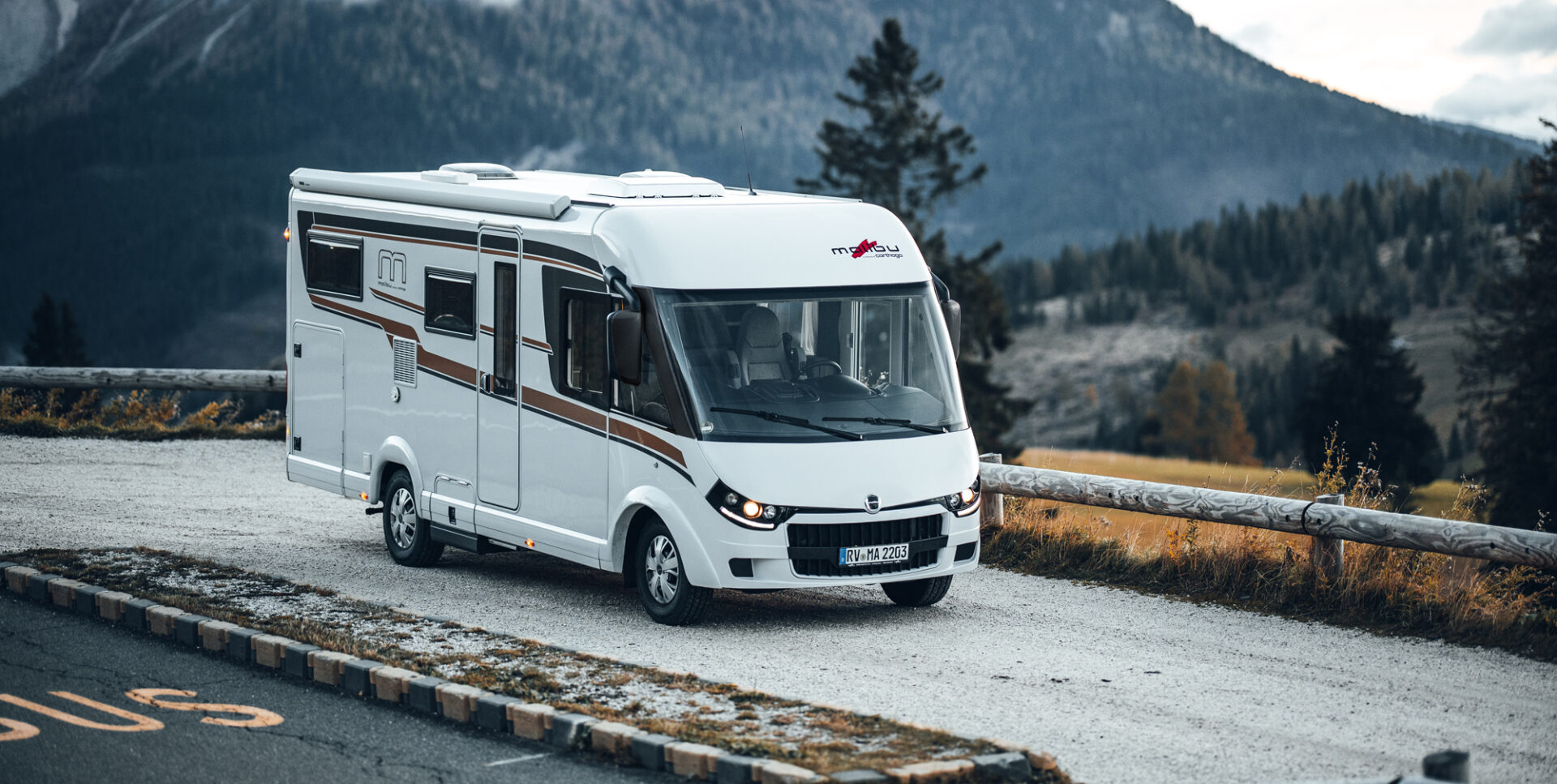 Vollintegriertes Malibu Wohnmobil in einer modernen Außenansicht, geparkt vor einer malerischen Kulisse mit Bergen im Hintergrund. Das Design des Wohnmobils betont seine aerodynamische Front und die großzügigen Fensterflächen.