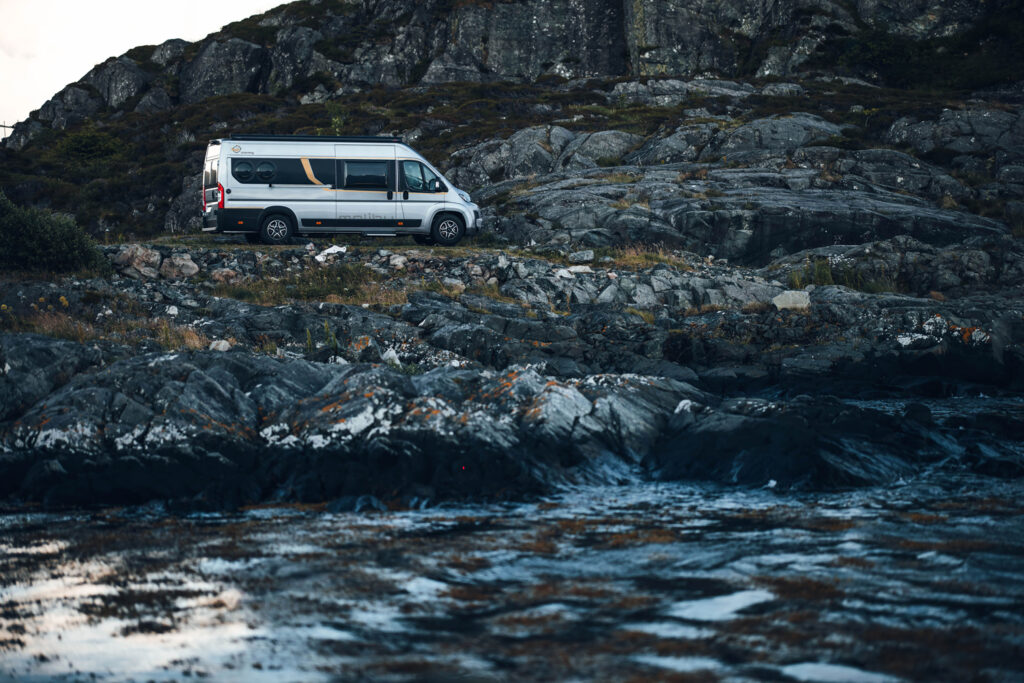 Malibu Wohnmobil geparkt an einer Küstenstraße in Italien, umgeben von einer malerischen Landschaft mit Meerblick und felsigen Klippen im Hintergrund.