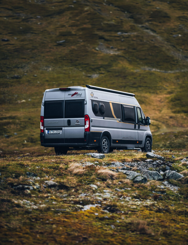 Seitliche Heckansicht eines Malibu Campervans auf einer felsigen Wiesenlandschaft.