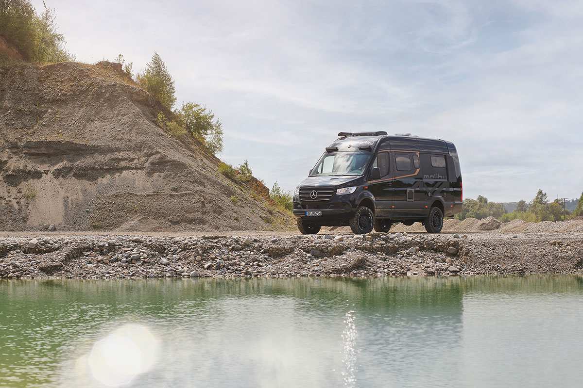 Malibu Genius 4x4 Performance, geparkt in einer bergigen Landschaft mit einer atemberaubenden Aussicht vor einem See, zeigt das robuste Design und die Geländetauglichkeit des Fahrzeugs in anspruchsvollem Terrain