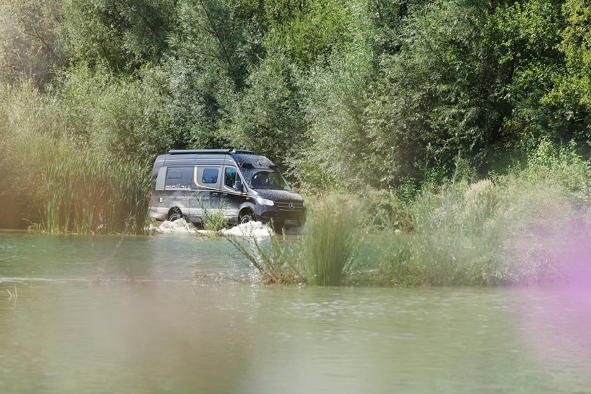 Malibu Genius 4x4 Performance in obsidianschwarz während der Fahrt durch einen kleinen See umgeben von Schilf, zeigt die Dynamik, Leistungsfähigkeit und das elegante Design des Fahrzeugs bei einer Tour durch die Natur.