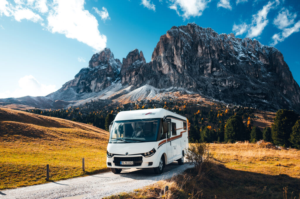 Ein vollintegriertes Malibu Wohnmobil fährt auf einer kurvigen Passstraße, umgeben von Bergen im Hintergrund.