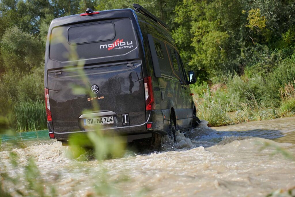 Malibu Genius 4x4 Performance in obsidianschwarz, fahrend durch hohes Wasser, umgeben von üppigem Grün, zeigt die Vielseitigkeit und Geländetauglichkeit des Fahrzeugs in natürlicher Umgebung.