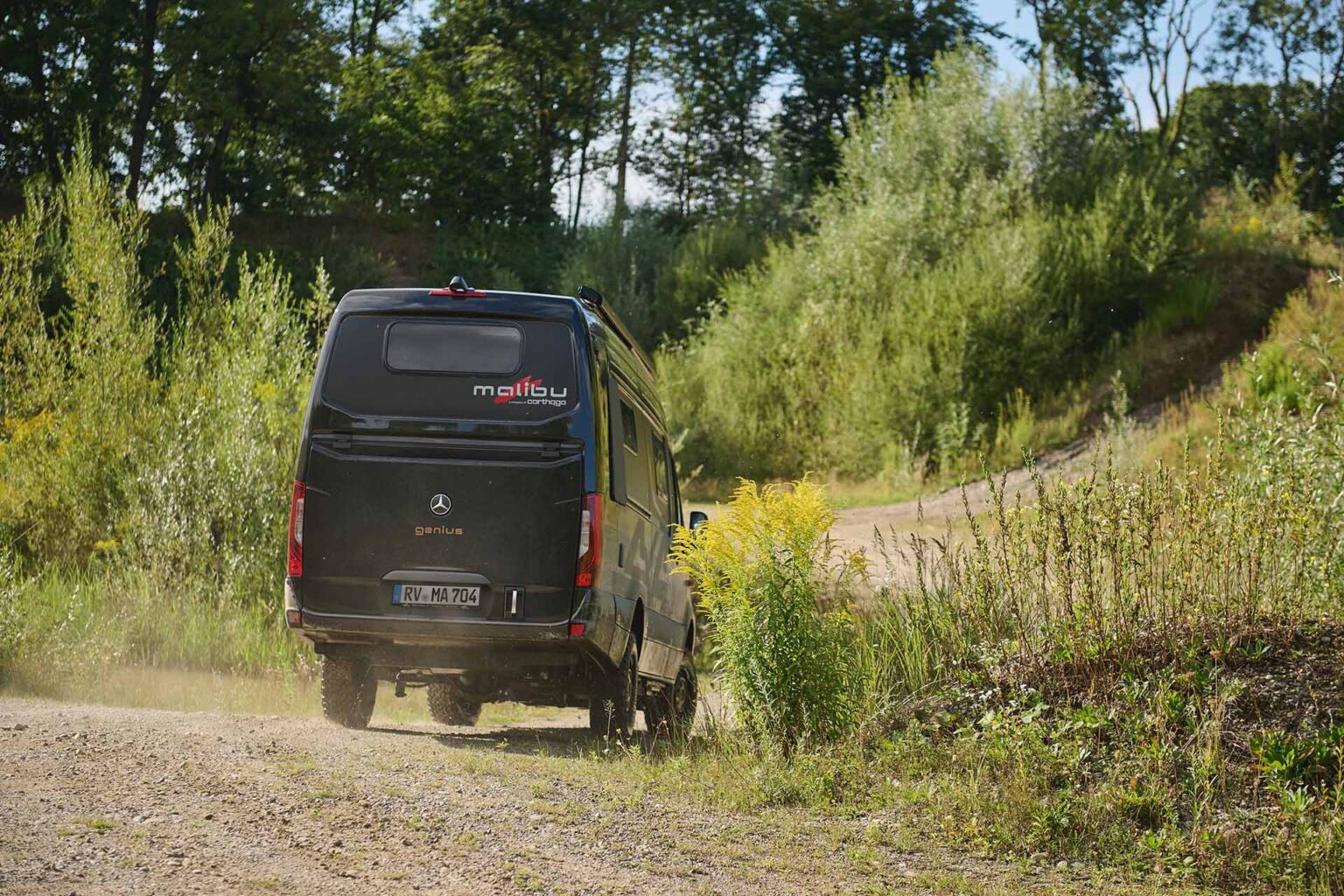 Malibu Genius 4x4 Performance in obsidianschwarz, Heckansicht, fahrend auf einem unbefestigten Gelände, zeigt die Offroad-Fähigkeiten und das robuste Design des Fahrzeugs in einer anspruchsvollen Umgebung